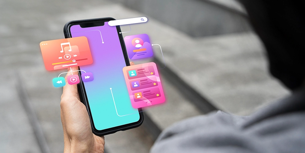A hand holds a smartphone with various interactive, colorful UI elements floating around it, showcasing the creativity of app developers.